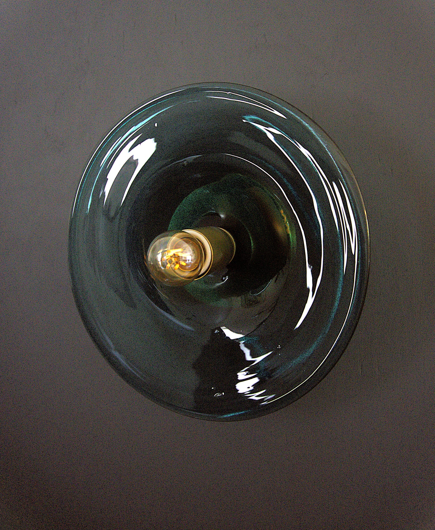 Glass light fixture with a visible bulb on a dark background. Blown glass wall sconce